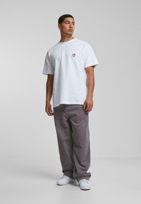 Hvid bomulds t-shirt med et lille rødt hjertegrafik, parret med grå kordfløjl bukser og hvide sneakers. Enkel, afslappet pasform design.