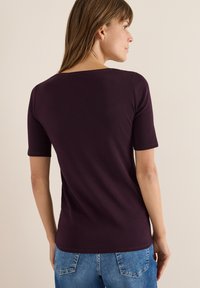 Bordeauxfarbenes kurzärmliges Shirt mit Rundhalsausschnitt, aus weichem, glattem Stoff gefertigt. Die Rückseite zeichnet sich durch ein einfaches, klares Design aus.