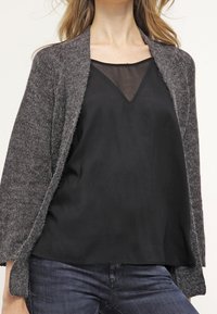 Harmaa neulejakku, jossa on avoin etuosa ja rento istuvuus, käytetty mustan, hihattoman, silkkisen toppi, yhdistettyinä farkkuihin.