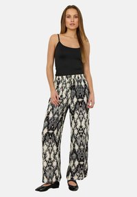 Top senza maniche nero abbinato a pantaloni larghi a fantasia in bianco e nero, con vita regolabile e tessuto leggero.