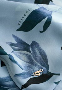 Heleda mustriga kangas helesinis toonis tumedate siniste lehtedega; äärtes on väike kuldne kone. Sile tekstuur.
