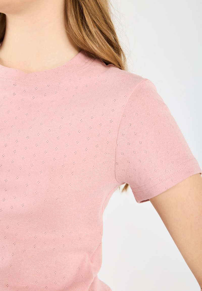 Lichtroze t-shirt met korte mouwen, voorzien van een textuurpatroon van kleine gaatjes, een ronde halslijn en een zachte, katoenachtige stof.