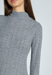 Maglione grigio a collo alto a coste con dettagli in perline metalliche, caratterizzato da un design aderente e maniche lunghe. Texture morbida e leggero lucido.