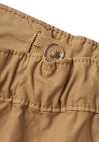 Ceinture en tissu beige avec une texture froncée, comportant un bouton en plastique transparent et des détails cousus. Bords plats et non finis.