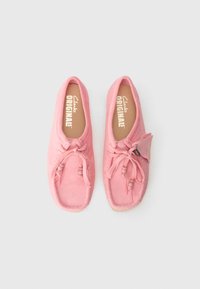 Pantofi slip-on din suede roz, cu vârf rotund, șireturi decorative, accente de mărgele și branț confortabil. Marca Clarks Originals este vizibilă în interior.