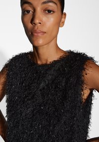 Top senza maniche nero realizzato in un tessuto texturizzato e morbido. Il materiale presenta fibre lunghe e sfibrate, creando un design distintivo e stratificato.