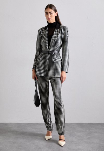 Mustvalge houndstooth-musteriga ülikond, millel on istuv bleiser, vöötatud talje ja kitsenevad püksid. Komplekti kuuluvad lamedate taldadega koorevärvi terava nina kingad ja must kott.
