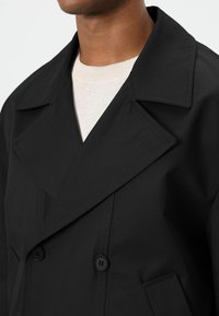 Zwarte double-breasted jas met een piek revers, twee knopen en een glad, lichtgewicht materiaal. Close-up van de kraag en textuur.