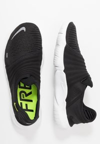 Czarne buty sportowe bez sznurowadeł z fakturowanym wierzchem, białą podeszwą i jaskrawozieloną wkładką z nadrukiem "NIKE FREE" w wyrazistym stylu.