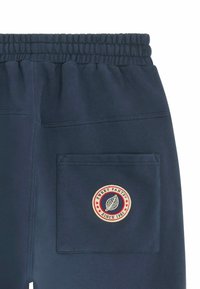 Pantalons de survêtement bleu marine en tissu doux, dotés d'une taille élastique, d'une poche latérale et d'un logo circulaire "Sweet Pants" en rouge et blanc.