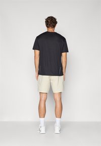 Camiseta deportiva negra de manga corta con cuello redondo, combinada con pantalones cortos beige claros, llevada con calcetines blancos y zapatillas deportivas.