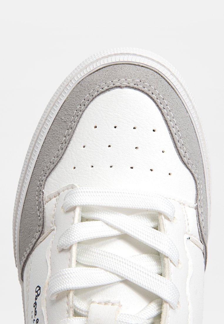 Zapatilla blanca con acentos grises, que presenta una parte superior de cuero suave, una caja de puntera perforada y cordones blancos. Suela de goma con un patrón texturizado.