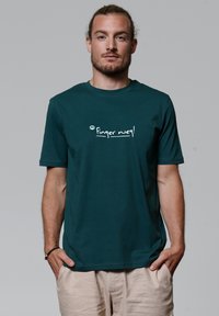 Teal katoenen t-shirt met korte mouwen met de tekst "Finger weg!" in het wit gedrukt op de voorkant. Eenvoudig ontwerp, relaxte pasvorm.