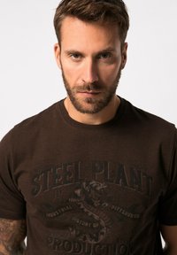 Brun bomulds t-shirt med et vintage grafiktryk af en slange og teksten "STEEL PLANT" i mørk blæk. Korte ærmer, crew neck design.