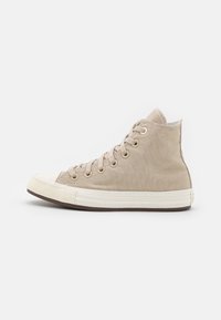 Beige high-top canvas sneaker with white rubber toe cap, lace-up front, metal eyelets, and a textured fabric finish. Features a classic silhouette.