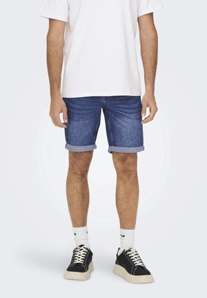 Krótkie spodenki jeansowe z podwiniętymi brzegami, średnio niebieski kolor, w połączeniu z białym t-shirtem i czarnymi trampkami z masywną podeszwą.