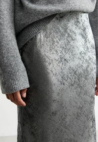 Pull en maille grise à manches longues associé à une jupe midi argentée brillante avec une surface texturée et des variations de motifs subtiles.