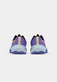 Sportsko med en lilla overdel og guldaccenter, en sort hælkant og en lyseblå mellemsål, designet til stabilitet og støddæmpning.