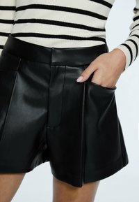 Černé kožené šortky s elegantním designem, texturovaným povrchem, plochými záhyby vpředu a boční kapsou. Stylizováno s pruhovaným svetrem.