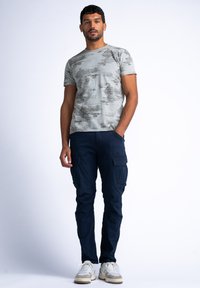 Grijze T-shirt met een subtiel patroon, gecombineerd met marineblauwe cargo pants met meerdere zakken. Witte en grijze sneakers maken de outfit af.