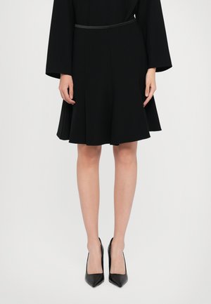 Black flared skirt with a smooth texture, featuring a fitted waistband. Paired with pointed black high-heeled shoes. Simple design.