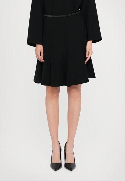 Falda negra acampanada con cintura ajustada, que presenta una textura suave. Combinada con tacones negros puntiagudos con un acabado texturizado.
