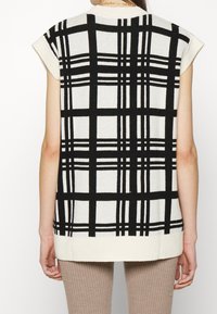 Haut sans manches en tricot à carreaux noir et blanc avec un col arrondi, un ourlet côtelé et des emmanchures larges, présentant une finition texturée.