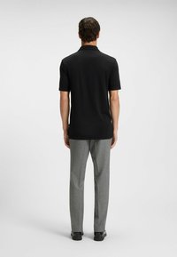 Czarna koszulka polo z krótkim rękawem widziana z tyłu, zestawiona z szarymi teksturowanymi spodniami i czarnymi butami. Prosty design, jednolity kolor.