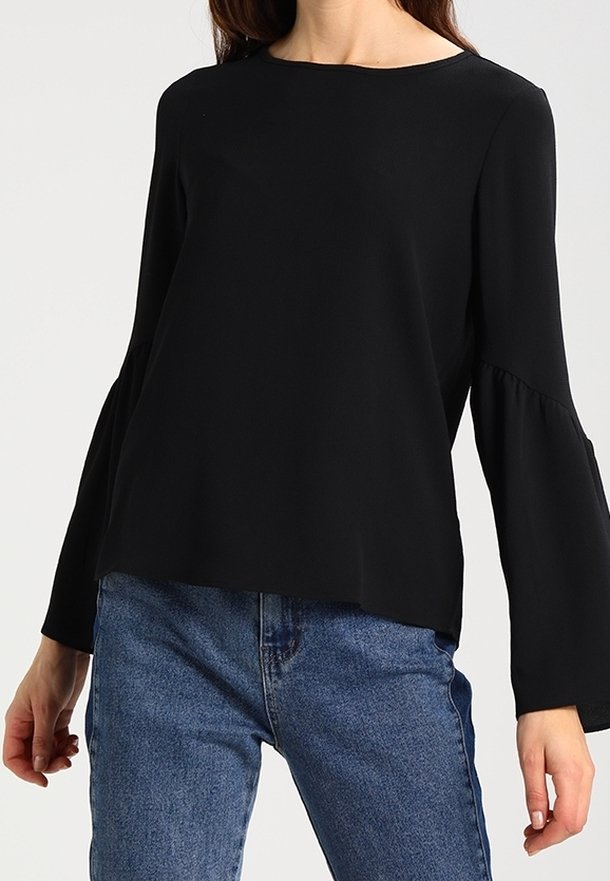 Top nero a maniche lunghe con scollatura rotonda e maniche a campana, realizzato in tessuto leggero. Abbinato a jeans blu.