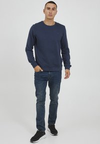 Navy sweatshirt with long sleeves, made of soft fabric, crew neckline, paired with blue jeans and black sneakers.