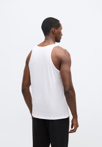 Maiou alb fără mâneci, cu gât rotund, realizat dintr-un material neted. Partea din spate prezintă un design simplu, fără modele sau accente.