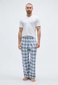 Tricou alb cu guler în V și logo-ul "Guess", asortat cu pantaloni de pijama albastru deschis cu carouri. Pantalonii au șnur și textură fină a materialului.