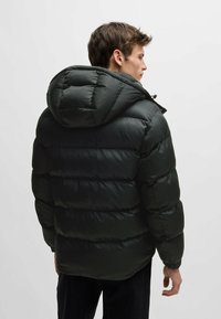 Svart puffjacka med en strukturerad yta, en snug huva och quiltad design. Materialet ser glansigt ut med elastiska cuffar för passform.