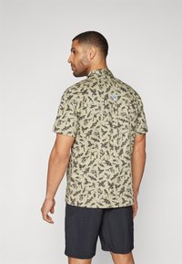 Korte mouw shirt in lichtgroen met een donker, door de natuur geïnspireerd patroon; heeft een kraag en een klein merkteken op de achterkant.