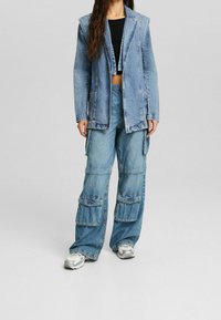 Světle modrá džínsová bunda se strukturovanými rameny, spárovaná s volnými džíny ve stylu cargo, které mají více kapes a uvolněný střih.