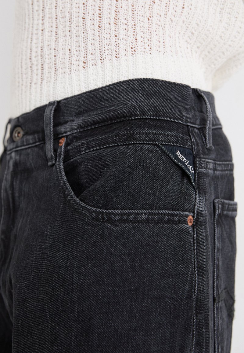 Schwarze Jeans aus Denim mit einem klassischen Fünf-Taschen-Design, das sichtbare Nähte und ein kleines Markenschild auf der Gesäßtasche aufweist.