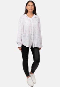 Witte overhemd met een roze hartpatroon, lichte stof, losse pasvorm; gecombineerd met zwarte glanzende leggings en witte sneakers.