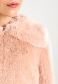 Rosa fuskpälsjacka med en plyschig textur och bred krage, med mjuka fibrer och en sömlös design, lämplig för avslappnad användning.