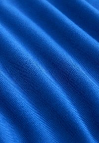 Tissu bleu texturé avec des lignes ondulées, mettant en avant une surface lisse et tricotée. La couleur est uniforme et vive, soulignant la profondeur et le motif.