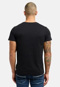 Sort bomulds T-shirt med klassisk rund halsudskæring, korte ærmer og en ensfarvet ryg. Synlige tatoveringer på armene, kombineret med blå jeans.