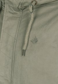 Veste matelassée vert clair avec capuche à cordon tressé et embouts métalliques argentés. Présente un logo brodé sur la poitrine.