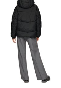 Schwarze Pufferjacke mit gestepptem Muster und Kapuze, kombiniert mit maßgeschneiderten grauen Hosen. Das Outfit hat eine lockere Passform und minimalen Hardware-Einsatz.