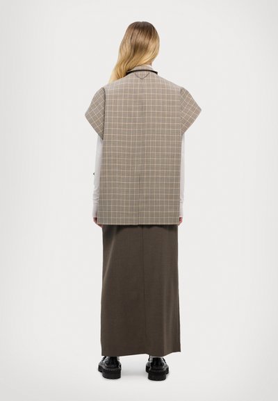Top a scacchi beige con maniche corte, sovrapposto a una lunga gonna marrone. Texture liscia con silhouette dritta, completato da scarpe nere.