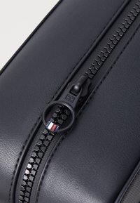 Čierna kožená taška s textúrovaným povrchom, vybavená čiernym zipsom a kruhovým ťahákom s červenými, bielymi a modrými akcentmi.