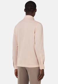 Ljust rosa långärmad skjorta med krage och knappade manschetter, med en slät tygtextur och en avslappnad passform.