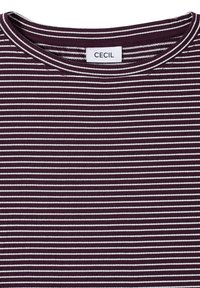 Närbild av en vinröd skjorta med tunna vita horisontella ränder och rund halsringning som har en liten "CECIL"-märkesetikett.