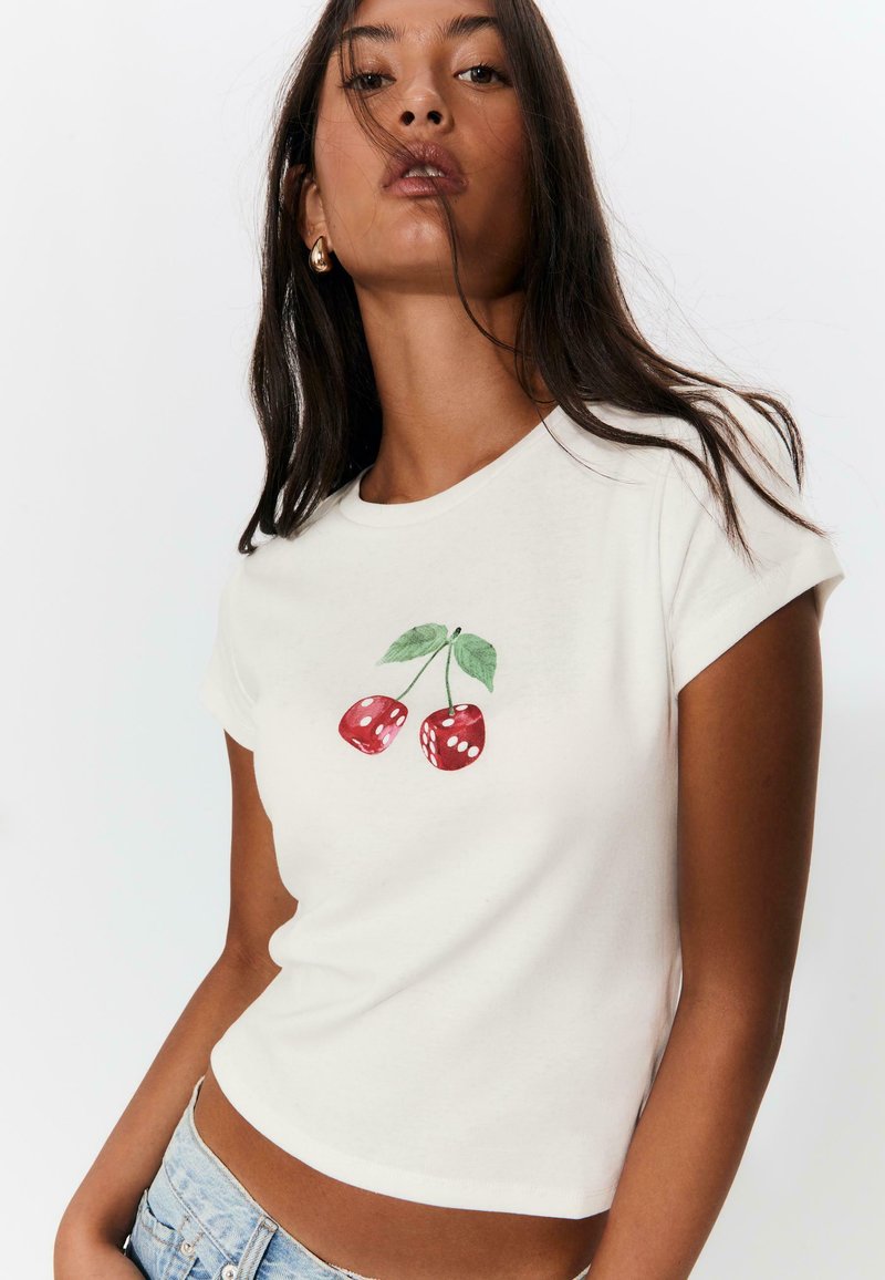 T-shirt bianco in cotone a maniche corte con ciliegie rosse e foglie verdi stampate sulla parte anteriore. Design aderente con scollatura rotonda.