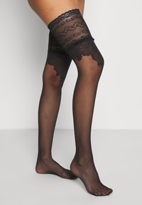 Sorte nettleggings til lårene med blonderkant øverst, med blomstermønster og teksturert design. Ingen synlige sømmer.