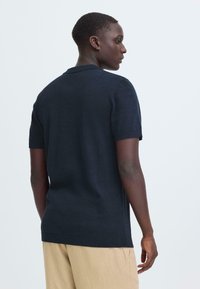 Polo à manches courtes bleu marine en tissu tricoté, doté d'un col, d'une finition texturée et d'une fente latérale à l'ourlet. Design uni, sans motifs.