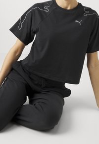 Camiseta negra corta con mangas cortas, con un sutil logo de Puma en gris y diseños de acento a lo largo de los hombros, hecha de una tela suave.